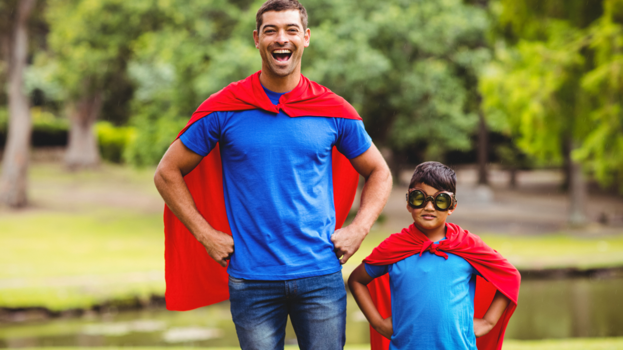 Padre e hijo sonriendo y vistiendo capas de superhéroe