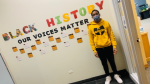 Young man stands next to wall that reads " Black History Our Voices Matter"