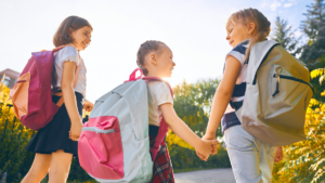 Young girls with backpacks on holding hands and smiling