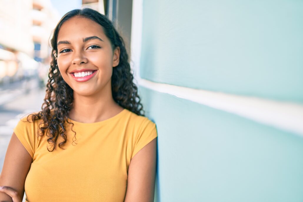 Young african american girl smiling happy leaning on the wall at city.