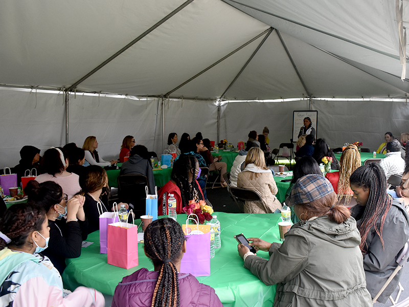 A large group of women are gathered under a tent and seated at decorated tables to encourage, mentor, and celebrate the young women that reside at Mercy Home's Walsh Campus.