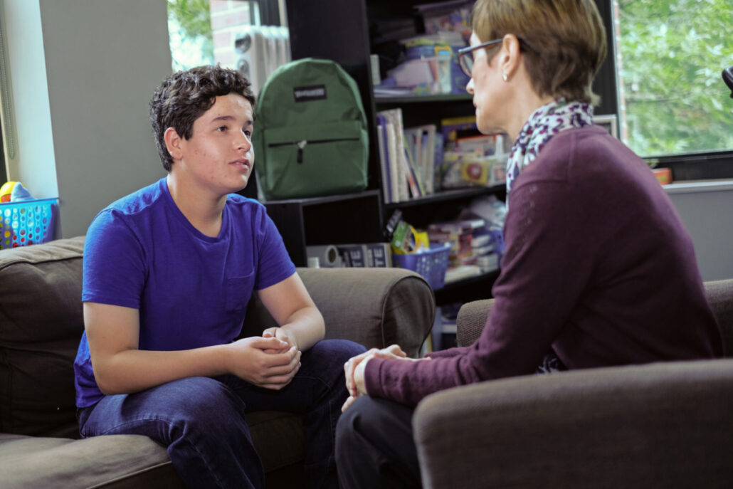 A boy sits with a therapist in a session