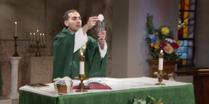 Fr. James Wallace raises a cup and a wafer ias he prepares the eucharist.
