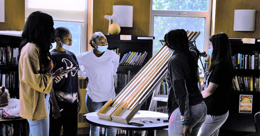 Mercy Home girls stand around a table and analyze a science experiment as they learn physics principles with ComEd.