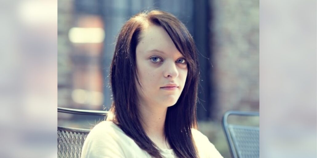 A sullen teenage girl looks unsmiling at the camera.