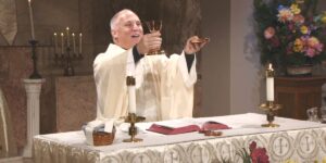 Dressed in a fine white robe, Fr. Jason Malave raises his hands to bless this week's communion as he leads the Sunday Mass community at Mercy Home in celebration of the Sunday of the Most Holy Trinity.