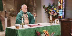 Fr. Malave lifts his hand to bless this week's communion as he leads the Sunday Mass community at Mercy Home in celebration of the Eleventh Sunday in Ordinary Time.