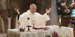 Fr. Malave raises hands to bless this weeks communion as he leads the Sunday Mass community at Mercy Home in celebration of the Most Holy Body and Blood of Christ.