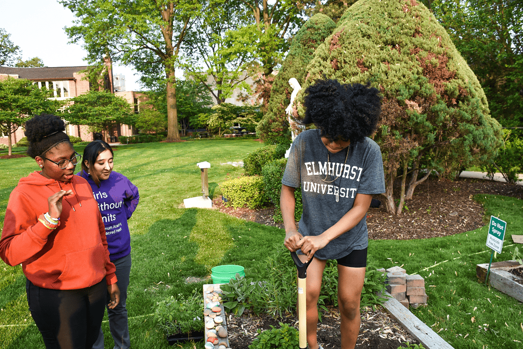 One of the girls shows the others how to dig a hole to plant flowers and seedlings.