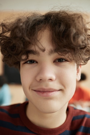 Close-up Verticle Portrait of a teenage boy, Alex, in school wearing a red and blue striped shirt and looking at the camera smiling.