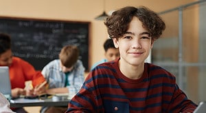 Portrait of a teenage boy, Alex, in school wearing a red and blue striped shirt and looking at the camera smiling.